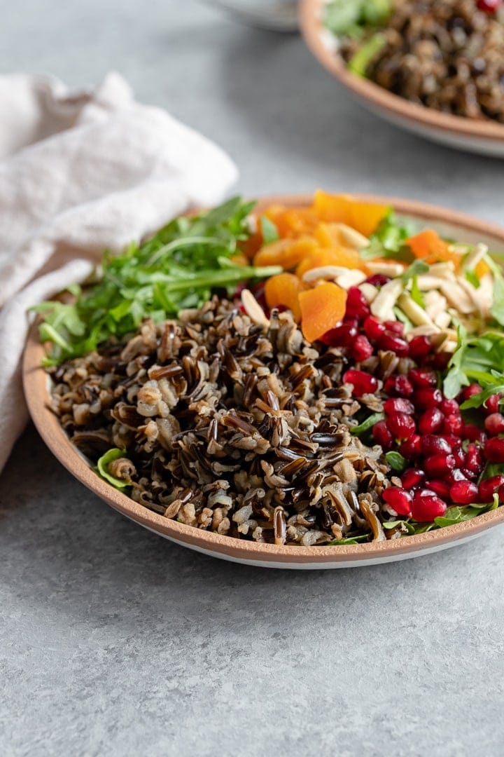 A bowl of wild rice winter salad with arugula, pomegranate arils, almonds, and dried apricots.