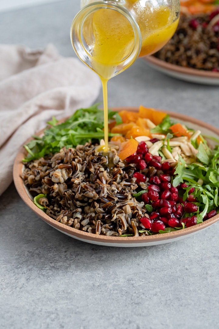 A cruet drizzling white wine vinaigrette onto a wild rice salad.