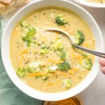 Spoon dipping into a bowl of broccoli cheddar soup.