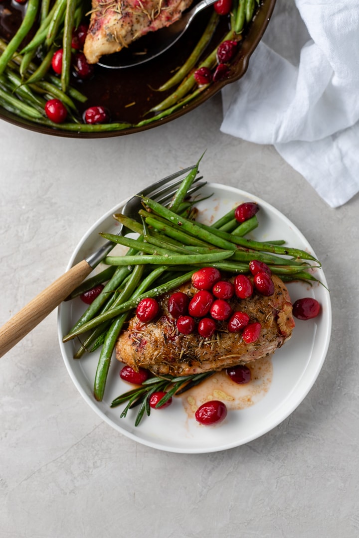 A white plate with a fork and one serving of cranberry chicken with green beans.
