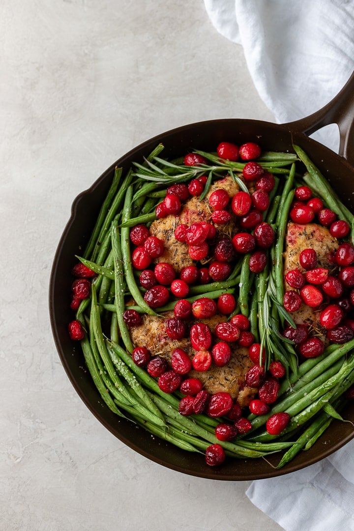 A cast iron skillet holding a meal of balsamic cranberry chicken with green beans, ready to serve.