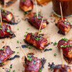 Close up of a chicken bacon BBQ bite slathered in BBQ sauce and garnished with chives.