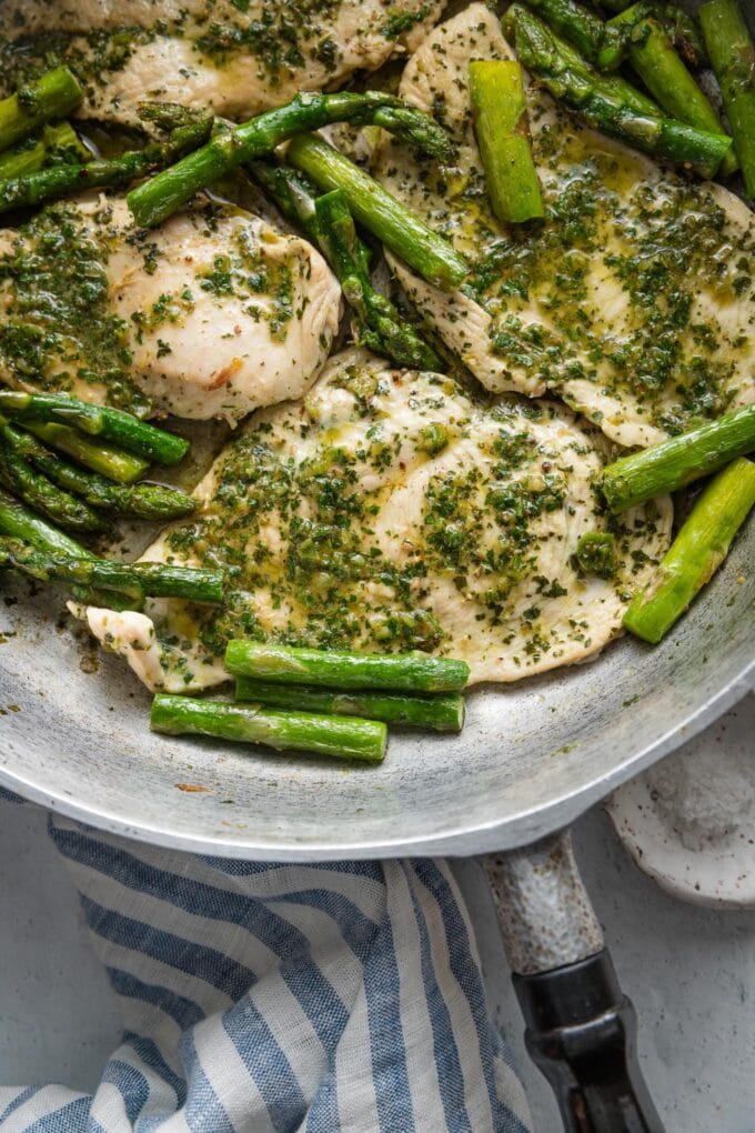 Overhead view of a deep sided cast iron skillet filled with thin-sliced chicken breasts sauteed in a homemade chimichurri sauce together with asparagus spears.