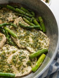 Skillet dish with thin sliced chicken breasts and asparagus spears cooked with a homemade chimichurri sauce.