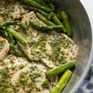 Skillet dish with thin sliced chicken breasts and asparagus spears cooked with a homemade chimichurri sauce.