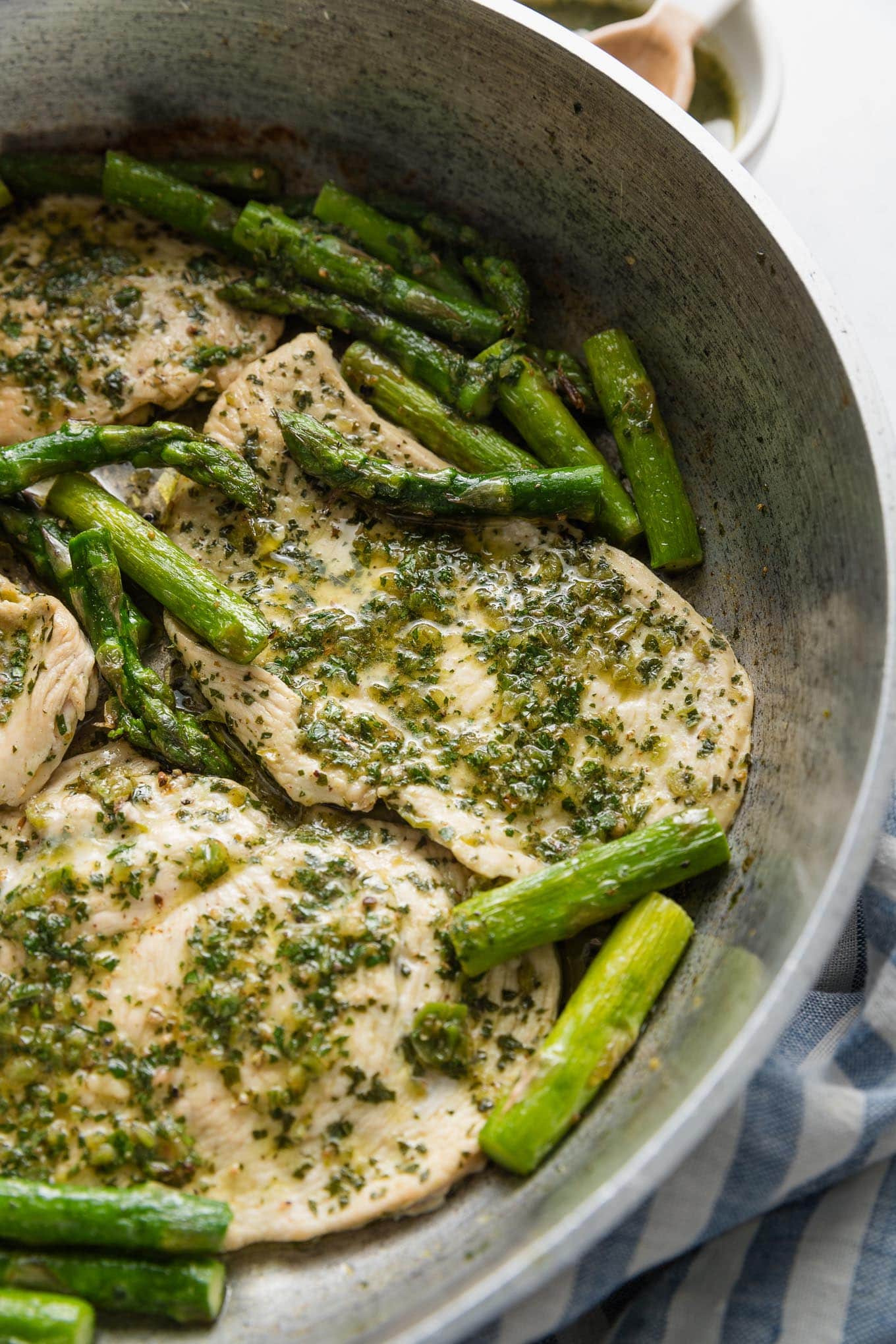Skillet dish with thin sliced chicken breasts and asparagus spears cooked with a homemade chimichurri sauce.