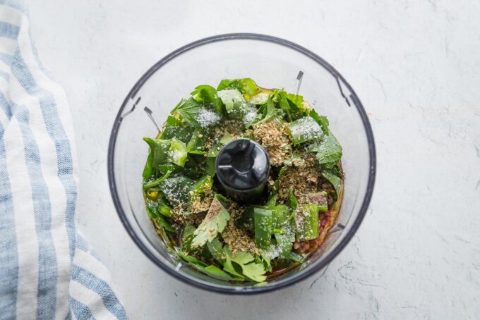 Chimichurri ingredients - fresh parsley, garlic, olive oil, red wine vinegar, pepper, salt, and black pepper - in a mini food processor ready to blitz.