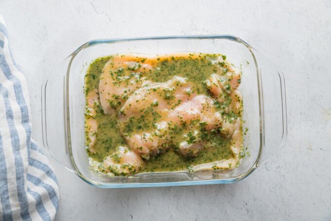 Thinly-sliced chicken breasts marinating in chimichurri sauce.