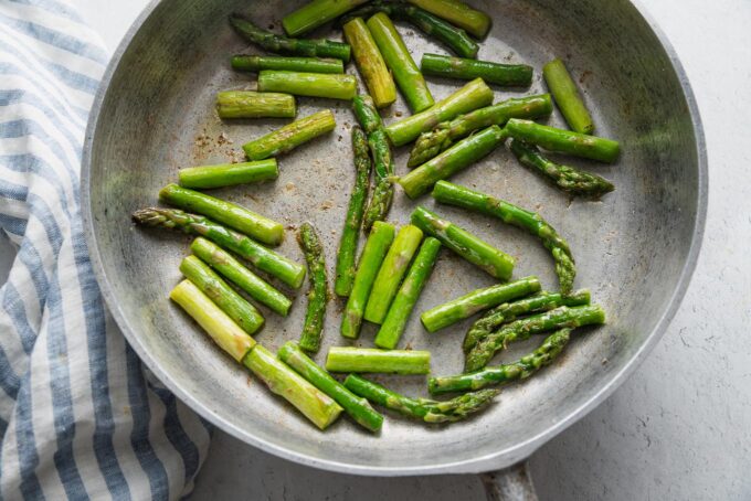 Chopped asparagus spears being sautéed in a cast iron skillet.