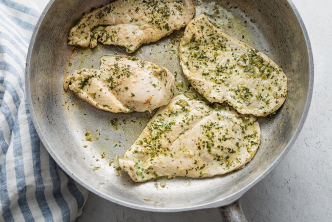 Chimichurri-marinated chicken breasts being cooked in a cast iron skillet.