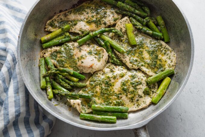 Asparagus and chicken breasts in a cast iron skillet cooked with chimichurri sauce.