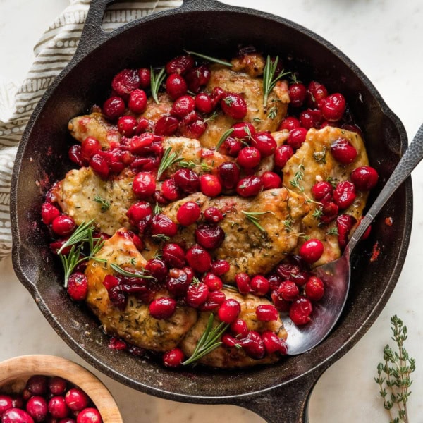 Cast iron skillet containing a balsamic cranberry chicken dish garnished with fresh thyme and rosemary.