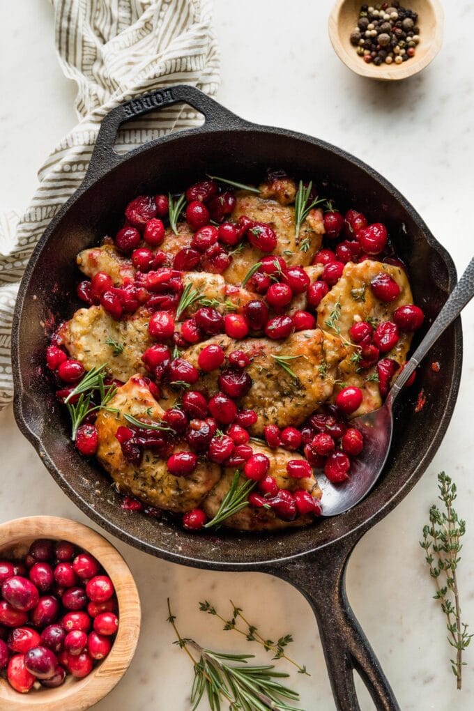 Cast iron skillet containing a balsamic cranberry chicken dish garnished with fresh thyme and rosemary.