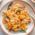 Close up of a bowl with a helping of Instant Pot risotto with butternut squash garnished with fresh sage leaves and crisped prosciutto.