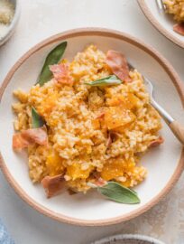 Close up of a bowl with a helping of Instant Pot risotto with butternut squash garnished with fresh sage leaves and crisped prosciutto.