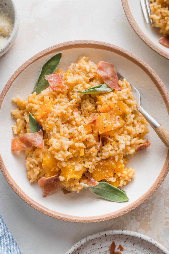 Close up of a bowl with a helping of Instant Pot risotto with butternut squash garnished with fresh sage leaves and crisped prosciutto.
