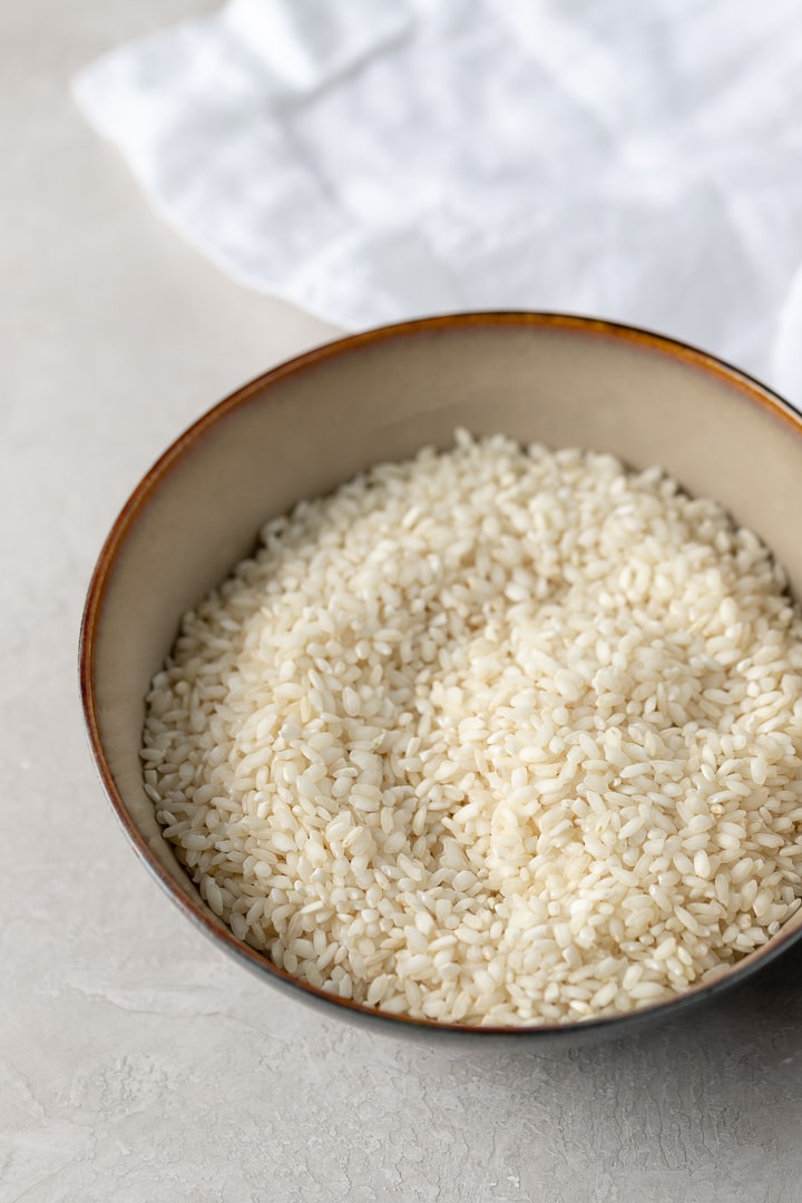 A close-up of Arborio rice grains in an earthenware bowl.