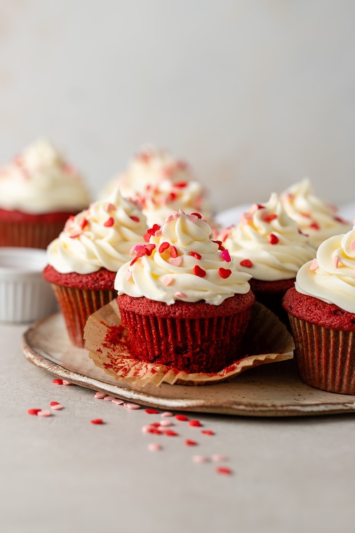 Close-up of an unwrapped red velvet cupcake with cream cheese frosting and heart sprinkles.