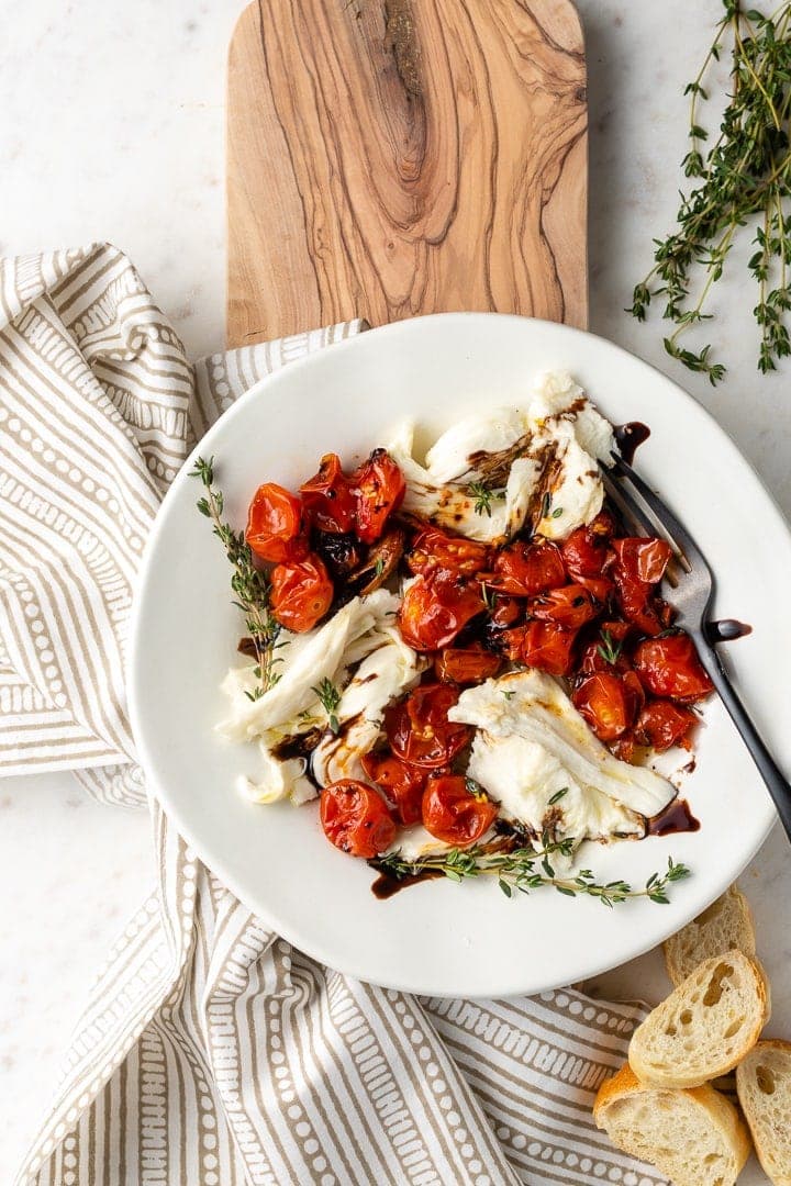 A white plate with a roasted tomato winter Caprese salad on it.