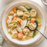 Bowl full of chicken tortellini soup with carrots, celery, parsley, and Italian herbs.