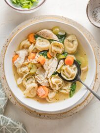 Bowl full of chicken tortellini soup with carrots, celery, parsley, and Italian herbs.