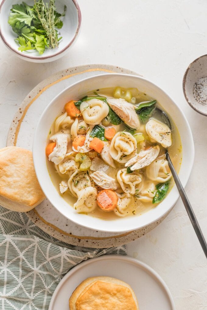 Bowls of chicken tortellini soup served with fresh parsley and buttery biscuits.