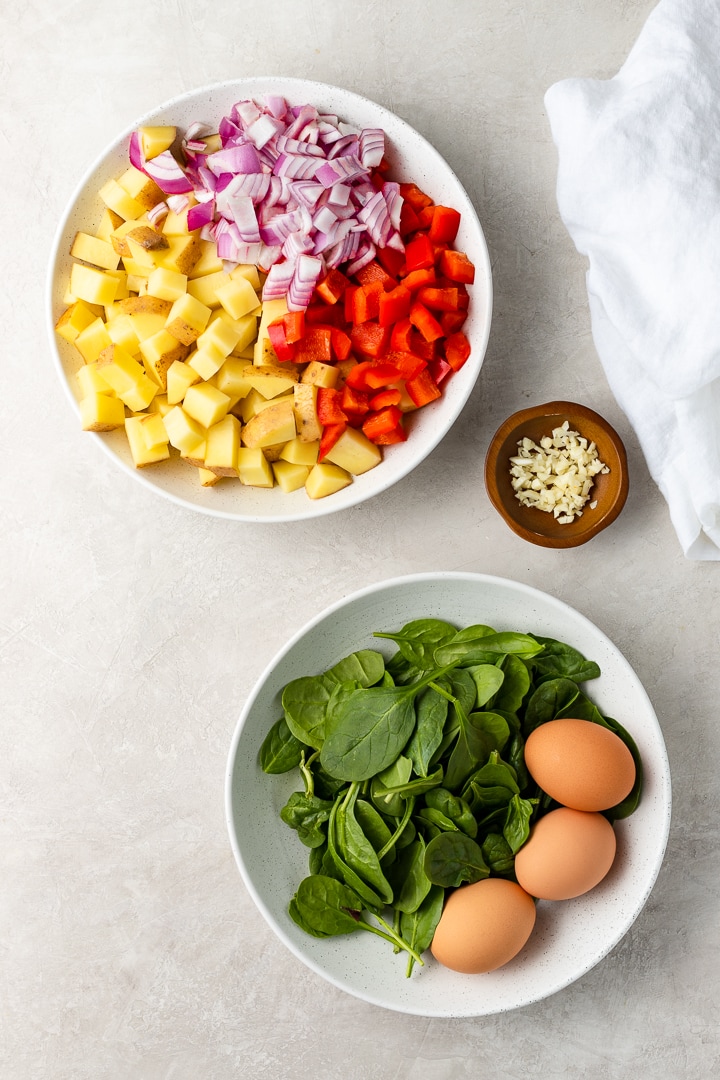 Bowls of chopped Yukon gold potatoes, red peppers, red onion, baby spinach, and eggs.