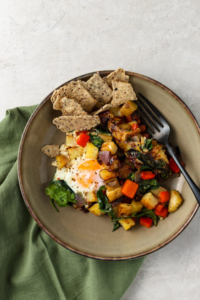 A small bowl filled with one serving of a crispy potato egg breakfast skillet and a handful of tortilla chips.