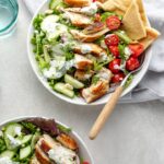 Prepared chicken gyro salad in a bowl with pita wedges and a fork.