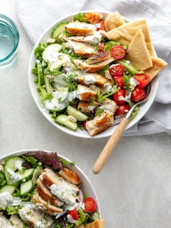 Prepared chicken gyro salad in a bowl with pita wedges and a fork.