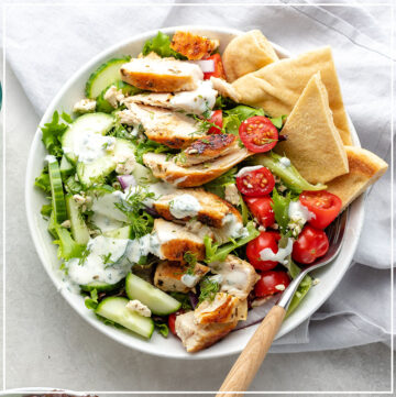 Prepared chicken gyro salad in a bowl with pita wedges and a fork.