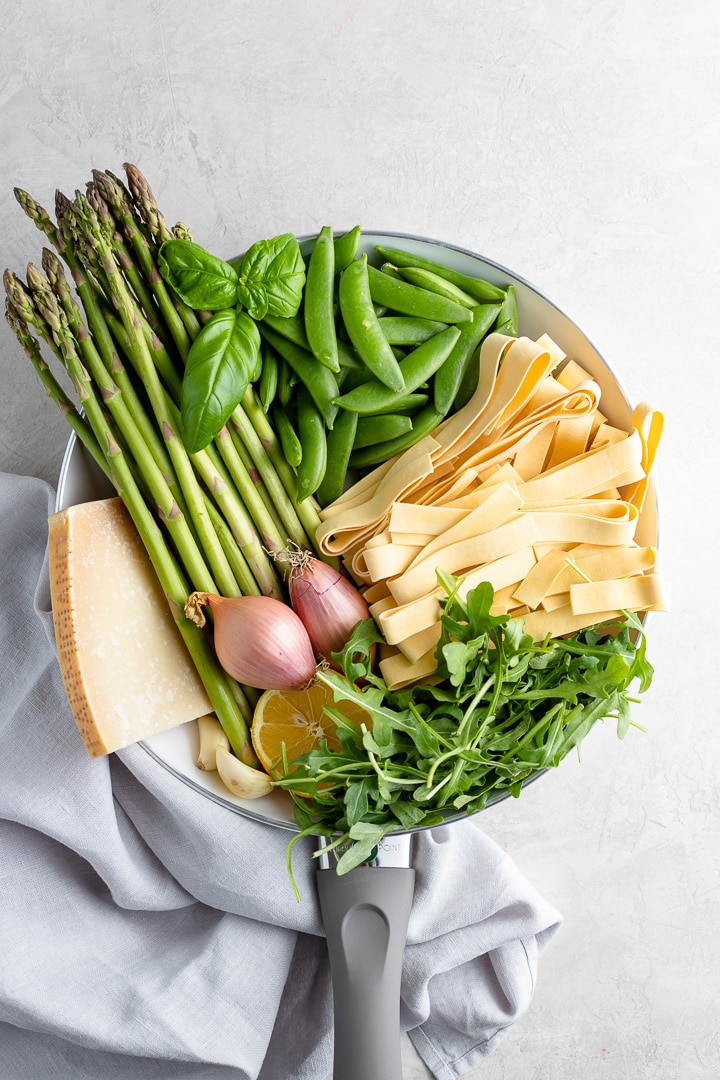 Ingredients for making a creamy pasta Primavera - asparagus, fresh basil, pappardelle noodles, peas, arugula, shallots, garlic, Parmesan cheese.