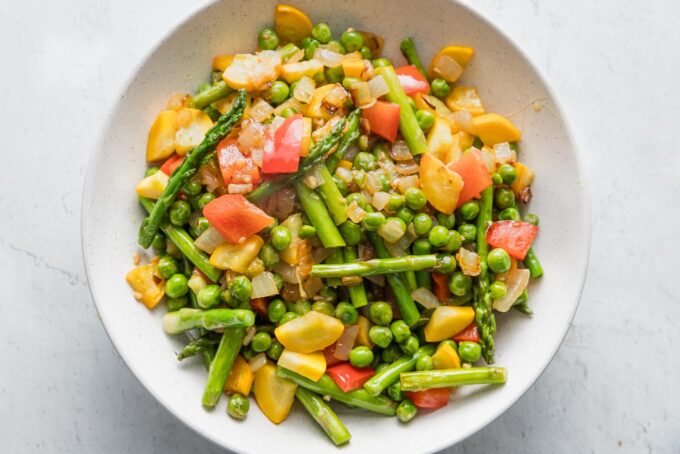 Bowl full of lightly sauteed vegetables: peas, asparagus, peppers, bell pepper, and onion.