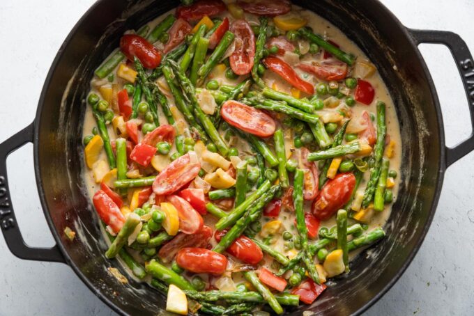 Large cast iron skillet filled with veggies in a light cream sauce.