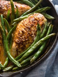 Close up of a cast iron skillet full of honey mustard chicken seared and baked with green beans.