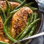 Close up of a cast iron skillet full of honey mustard chicken seared and baked with green beans.