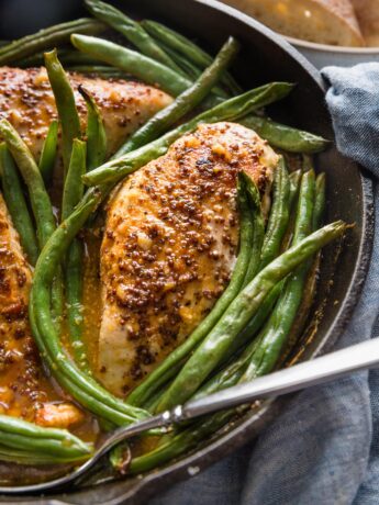 Close up of a cast iron skillet full of honey mustard chicken seared and baked with green beans.