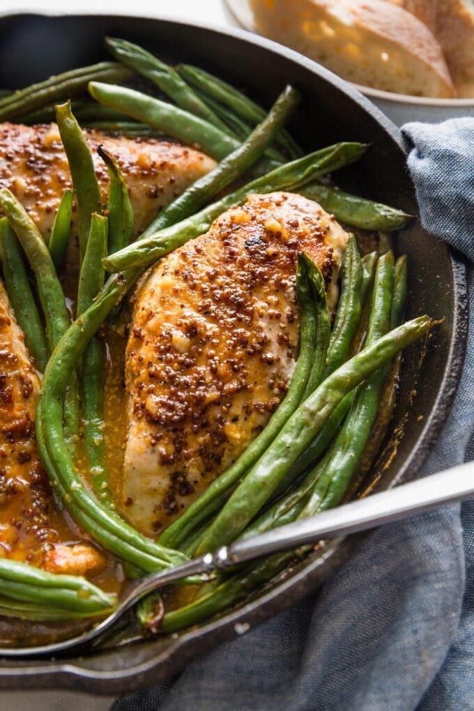 Close up of a cast iron skillet full of honey mustard chicken seared and baked with green beans.