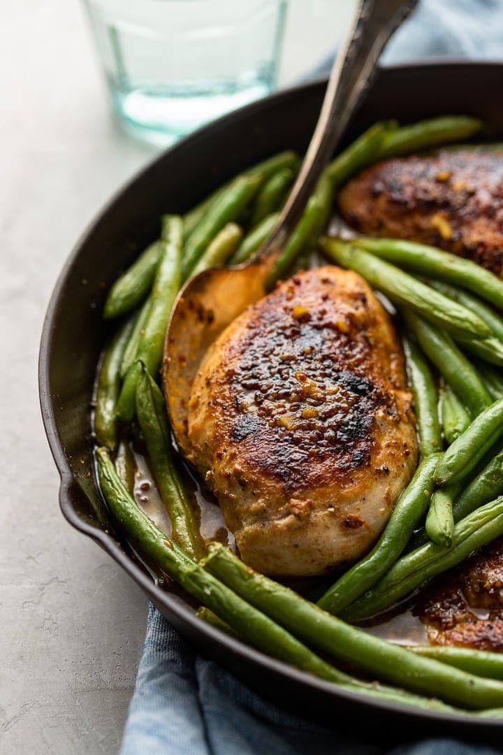 Close-up of honey mustard chicken cooked in a skillet with green beans.
