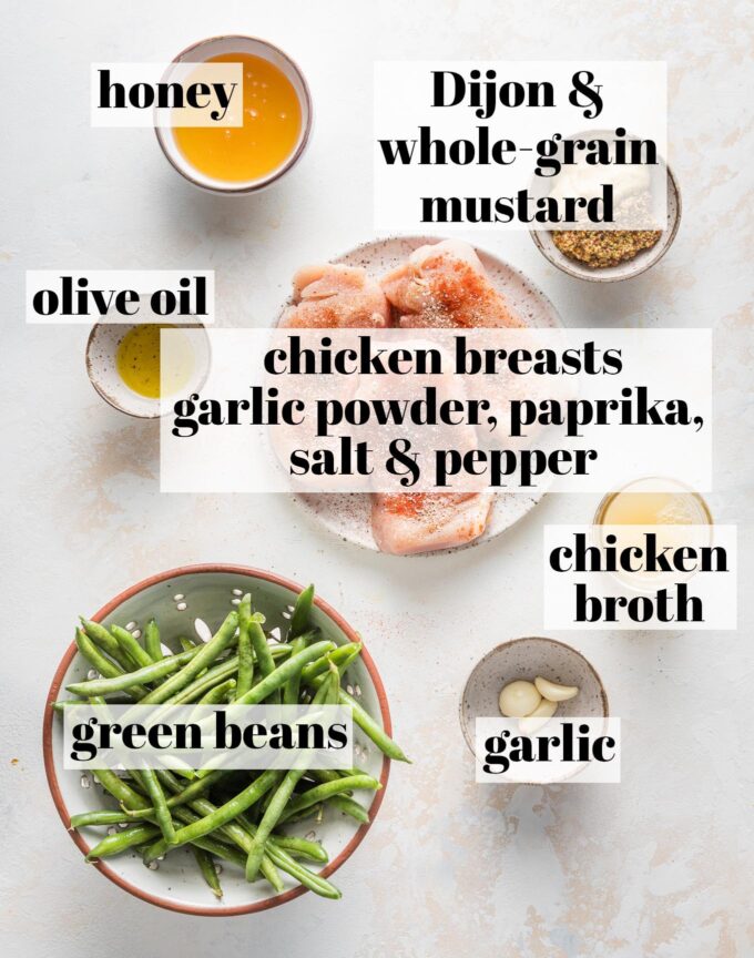 Labeled overhead image of chicken breasts sprinkled with garlic powder, paprika, salt, and pepper; honey, Dijon mustard, whole grain mustard, olive oil, chicken broth, green beans, and minced garlic, all measured into prep bowls and ready to cook.