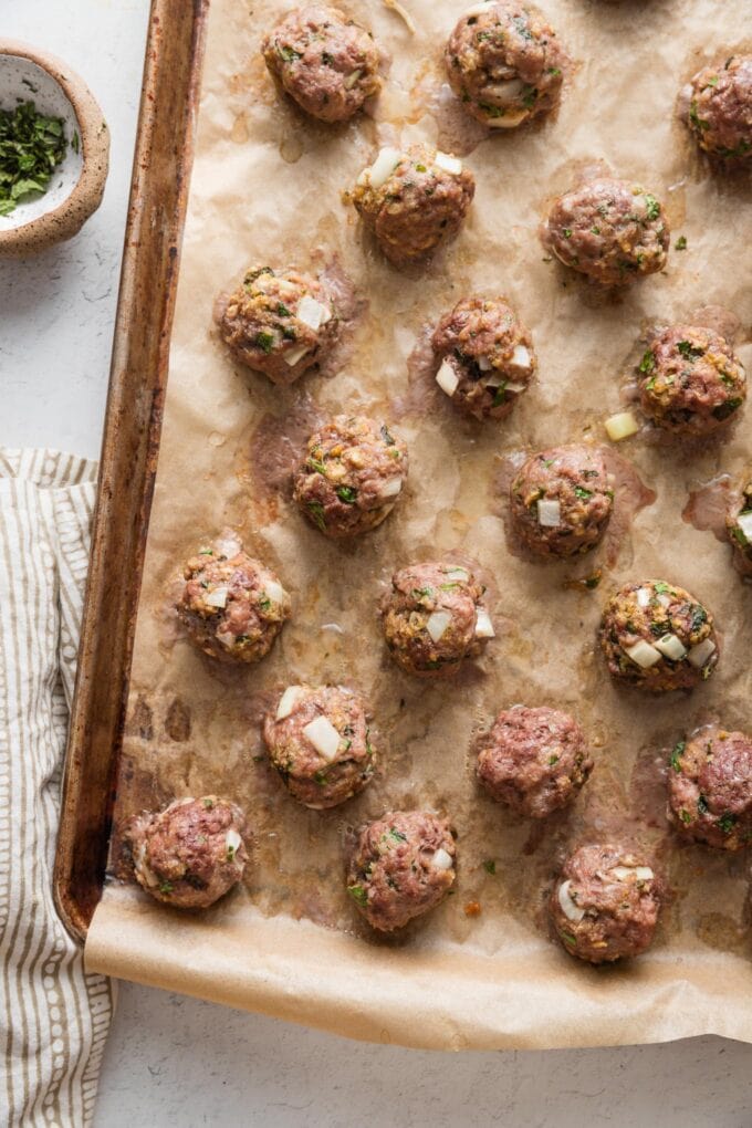 Sheet pan full of baked Moroccan-inspired lamb meatballs, just removed from the oven and cooling on the counter.