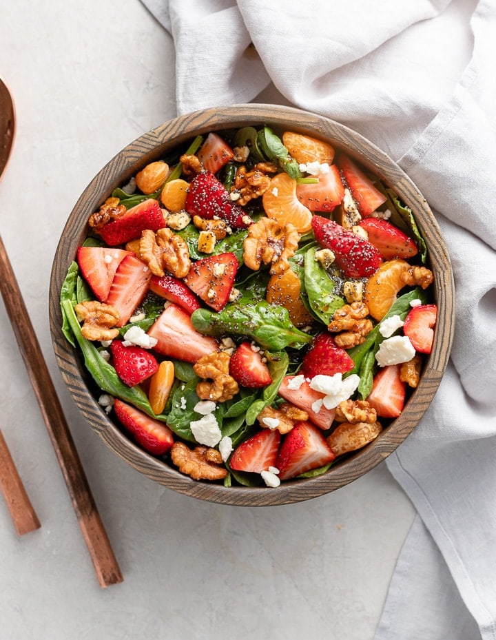 Overhead image of an easy strawberry spinach salad, with feta, oranges, candied walnuts, and a balsamic poppy seed dressing.