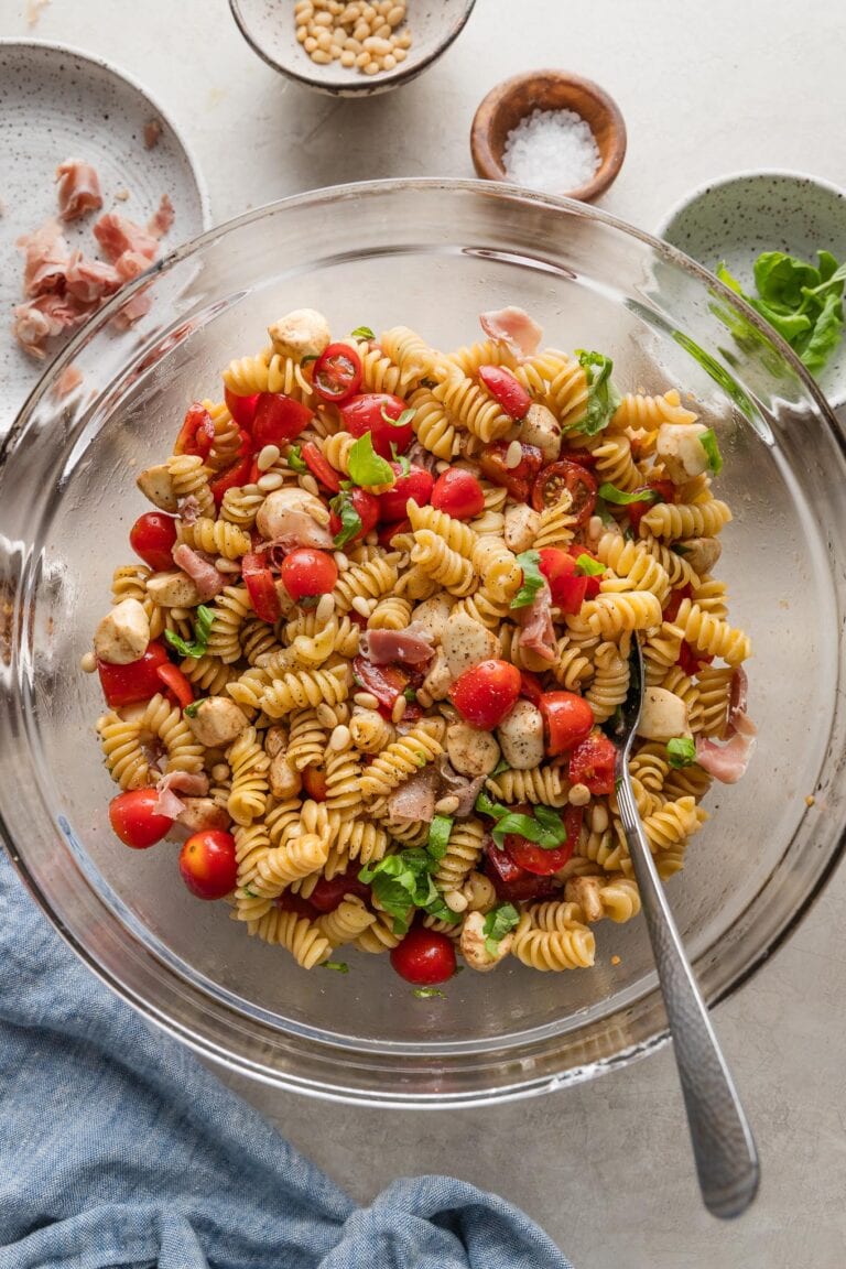 Bowl full of Caprese pasta salad with fresh mozzarella, tomatoes, fresh basil, prosciutto, pine nuts, and a homemade balsamic dressing.