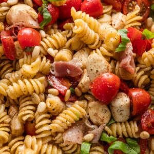 Close up of a caprese pasta salad with prosciutto and pine nuts.