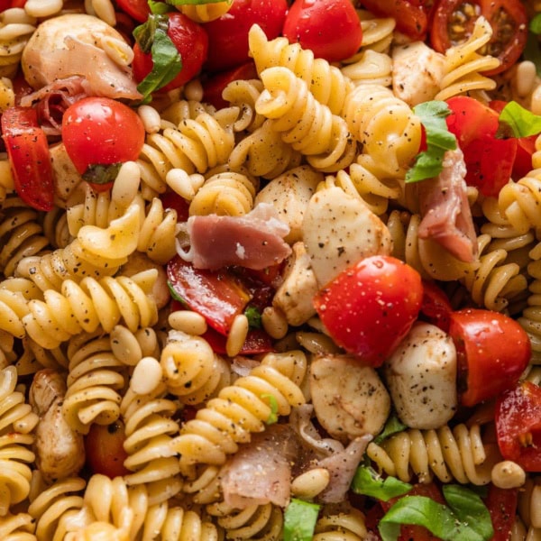 Close up of a caprese pasta salad with prosciutto and pine nuts.