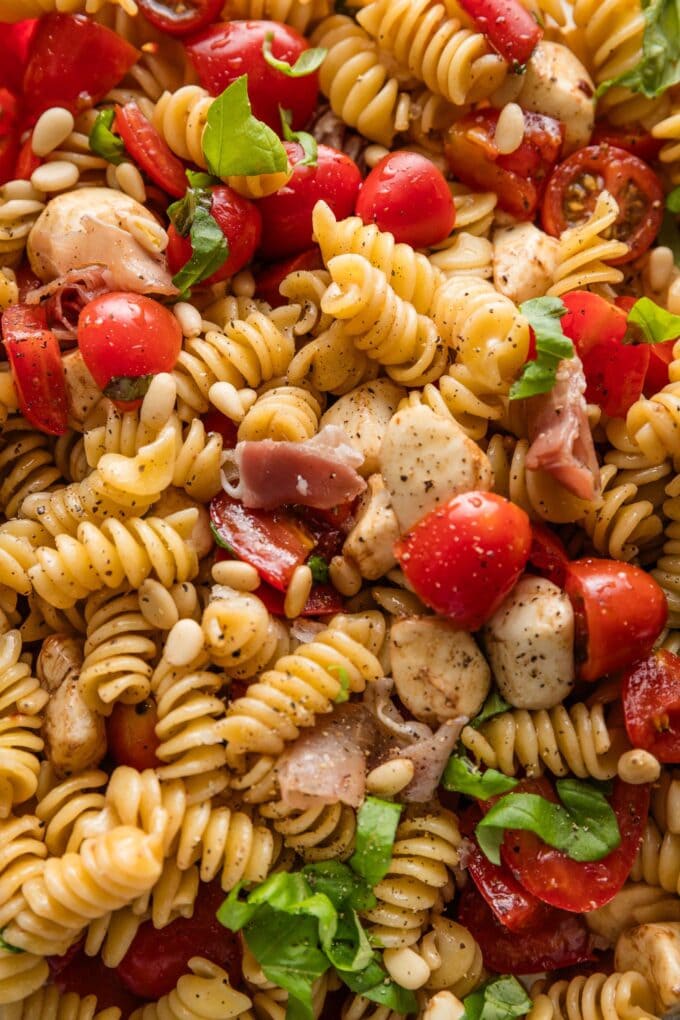 Close up of a caprese pasta salad with prosciutto and pine nuts.