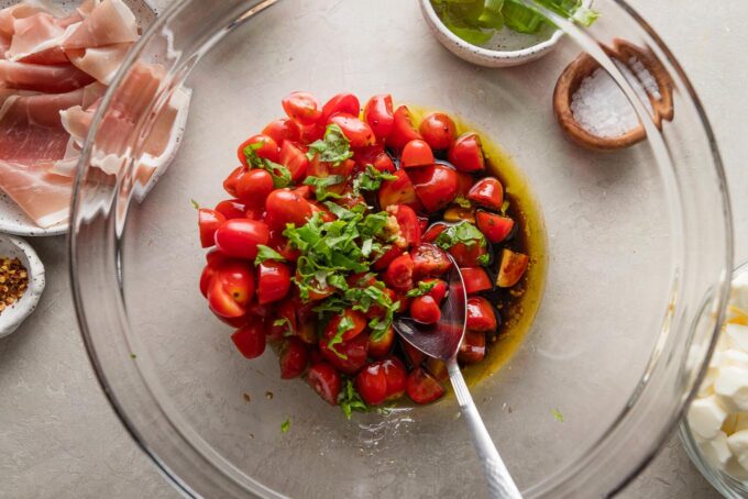 Bowl full of halved cherry tomatoes, fresh basil, minced garlic, balsamic vinegar, and olive oil.
