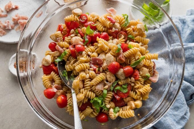 Caprese pasta salad with prosciutto, pine nuts, and fresh basil on top.
