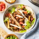 Plate with ground beef tacos and Instant Pot in the background.