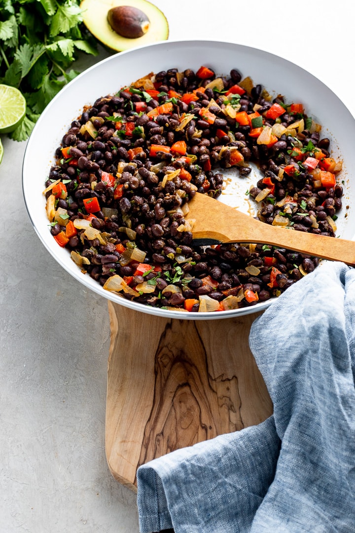 A wooden spoon stirring black beans in a skillet.